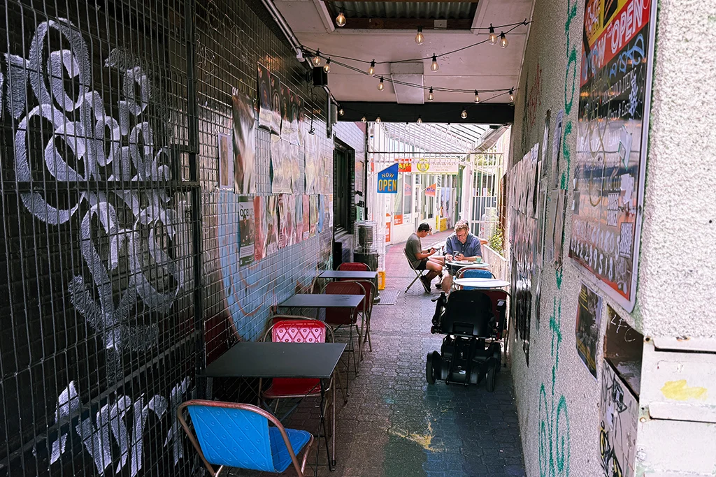 An alley in Moonah with cafe seating, festoon lighting, gig posters and graffiti. Patrons sit and enjoy a coffee.