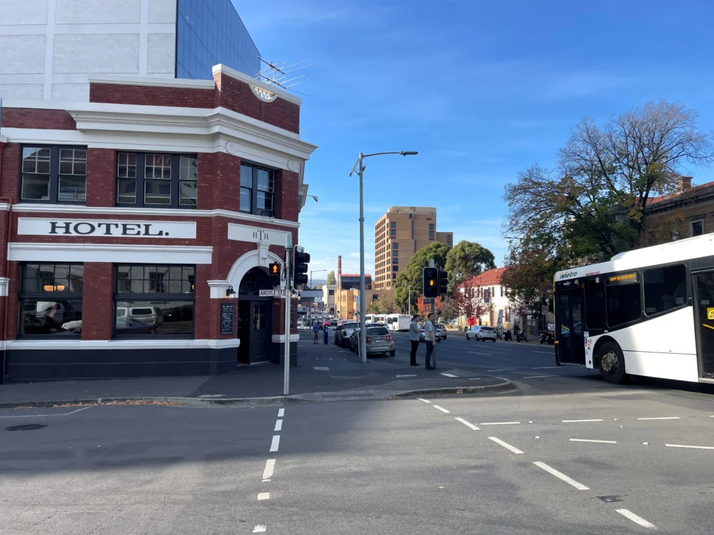 A Metro Tasmania bus drives past Hobart Town Hotel. People wait at the crosswalk.