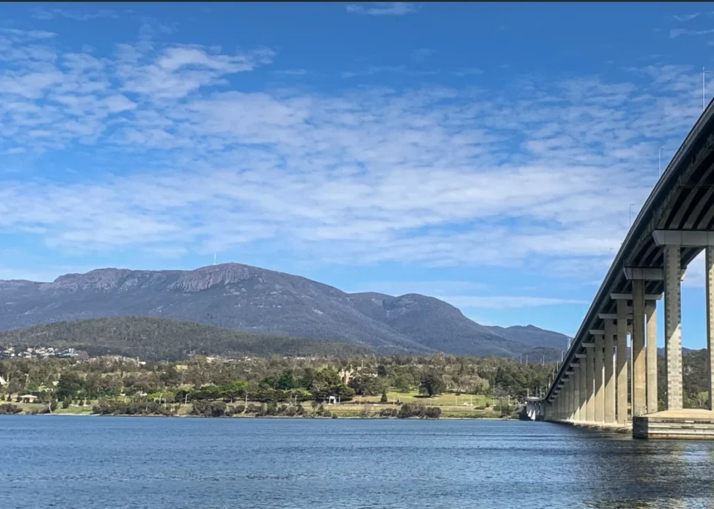 A view of Kunanyi (Mount Wellington) taken from the Eastern Shore with the Tasman Bridge on the right and the river pictured in the foreground.