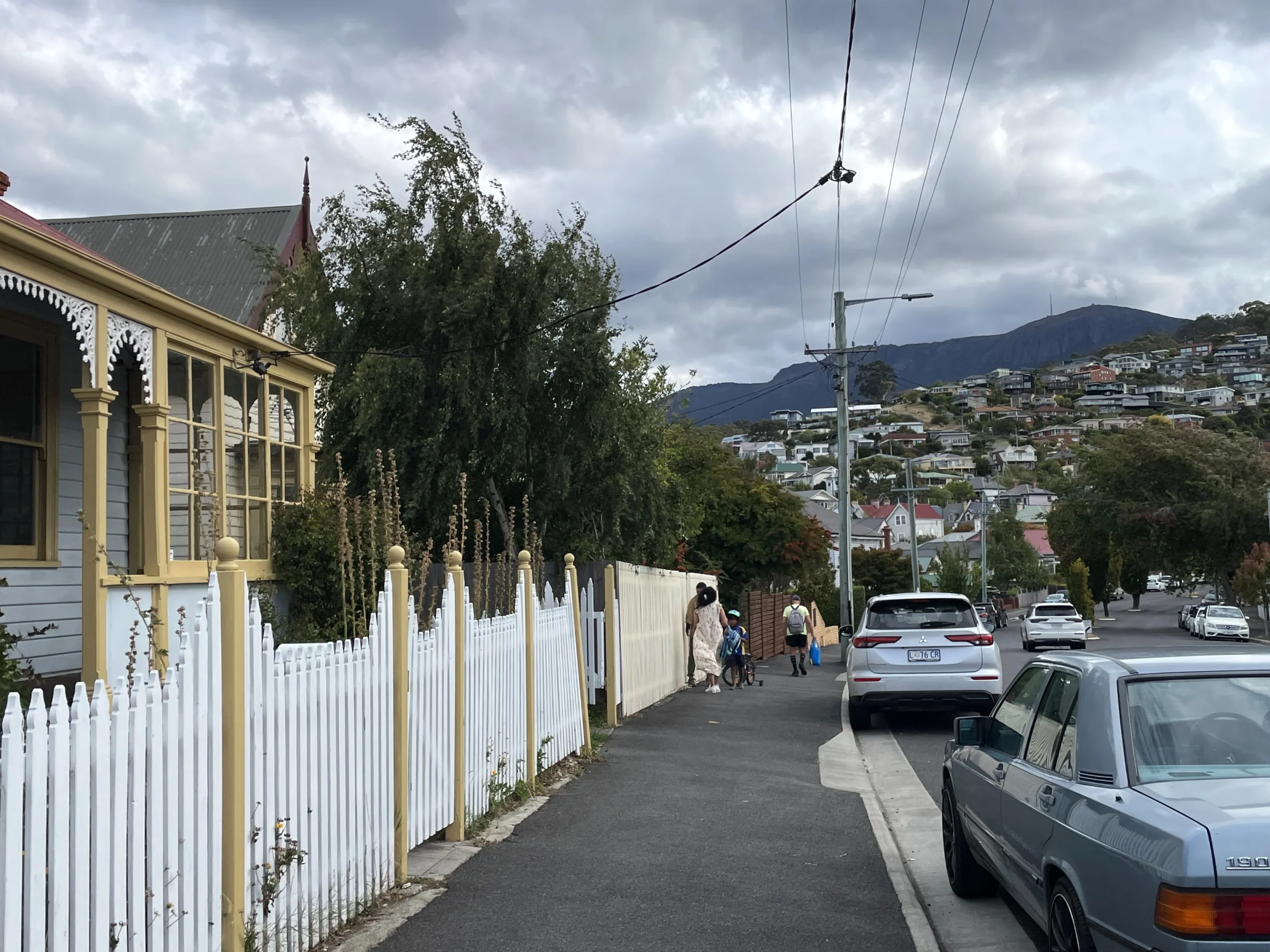 A family walks on the footpath next to a cottage in West Hobart