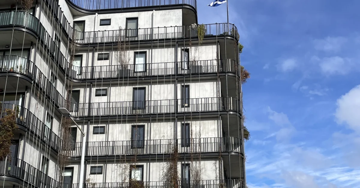 The Commons, a mid-rise housing option in the Hobart CBD. The building shown has curved balconies, plants growing on its exterior and a flag flying on the second top balcony.