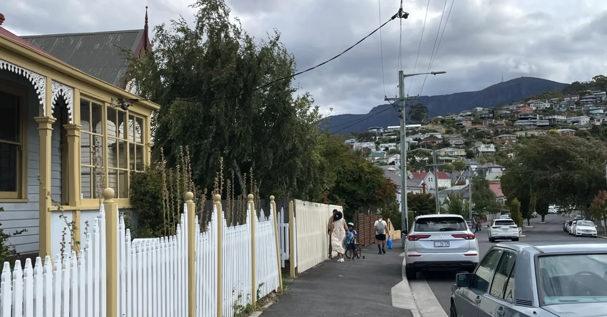 A family walks on the footpath next to a cottage in West Hobart